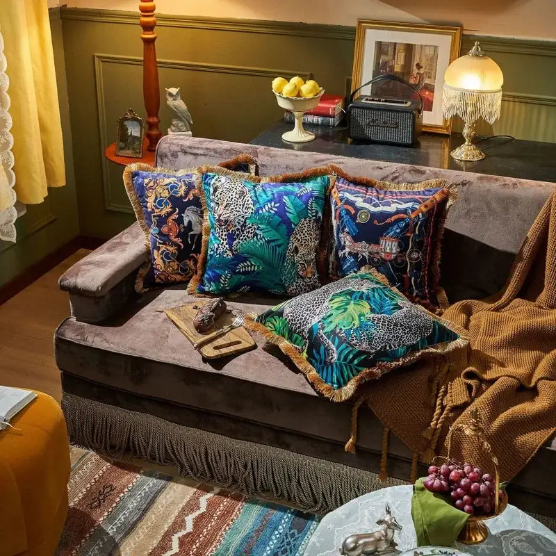 Four luxury cushion covers with gold fringe and jungle animal collection motifs in teal and blue on gray velvet sofa