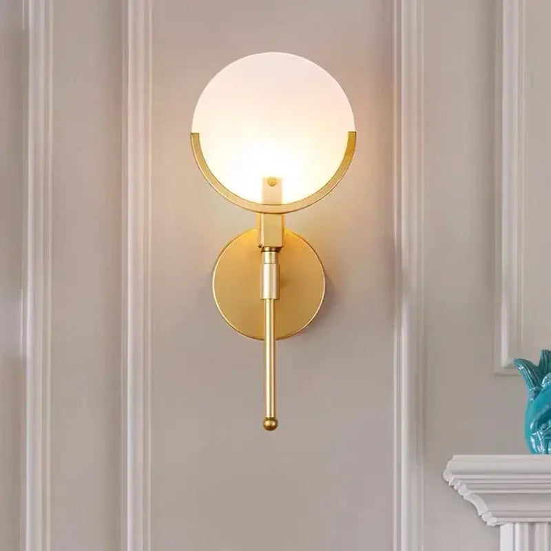 Gold-toned copper wall lamp with frosted glass globe and circular base from decorbites marble collection for bedroom decor