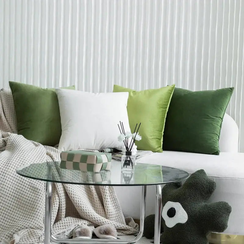 A sleek glass-top coffee table with chrome legs paired with luxury olive green decorbites green velvet pillow case