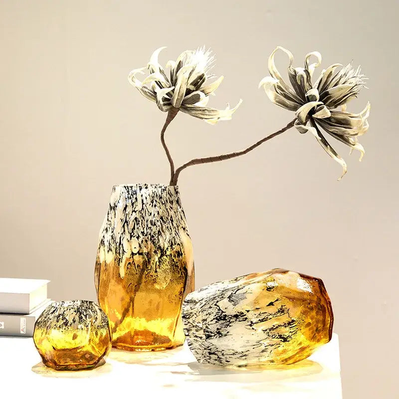 A set of three amber gradients black glass vases with marbled patterns including a tall black glass vase with artificial flowers