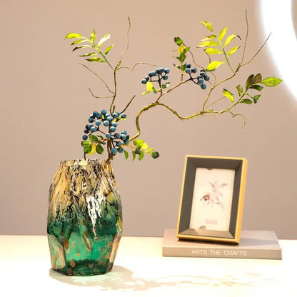 A marbled green and black glass vase with swirling gold gradients black glass holds branches with blue berries for decorbites gradients black