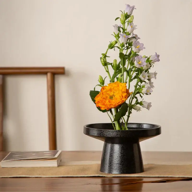 Matte black ceramic vase sword mountain with flared rim holding white bellflowers and orange ranunculus decorbites ceramic vase