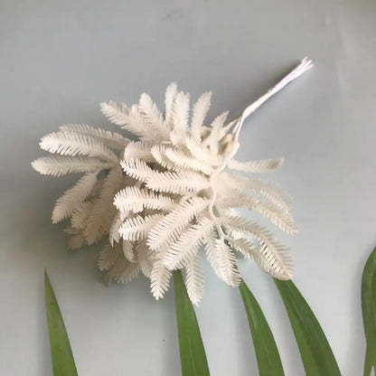 White plastic fern-shaped floral hair accessory with thin wire stem alongside metallic silver gold and white artificial eucalyptus leaf bunch