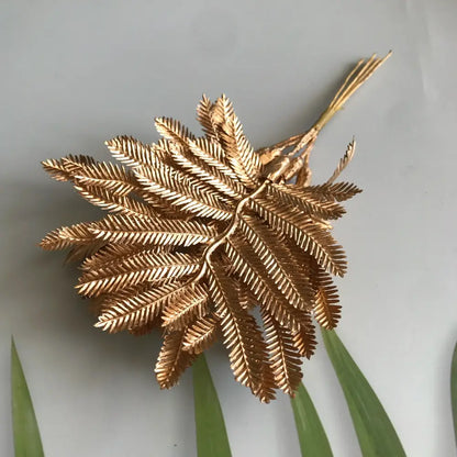 Golden metallic fern brooch with intricate leaf detailing displayed alongside artificial eucalyptus leaf branches for living room decor