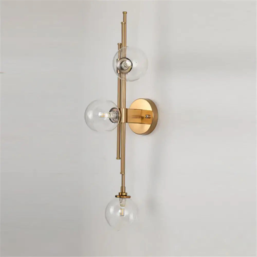 Mid century brass finish 3 light wall sconce with clear glass orb shades vertically arranged along slender arm