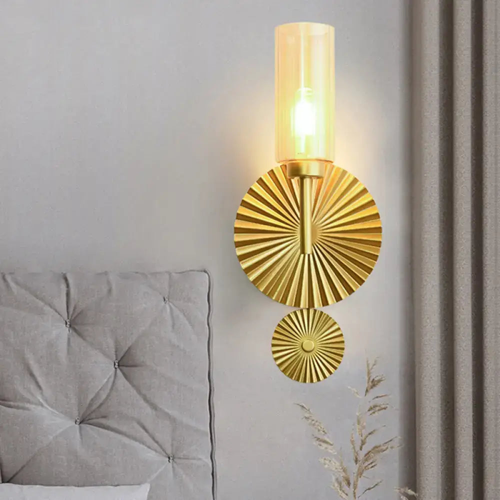 Gold-finished mid century wall sconce with scalloped brass backplate and amber cylindrical glass shade for bedroom use