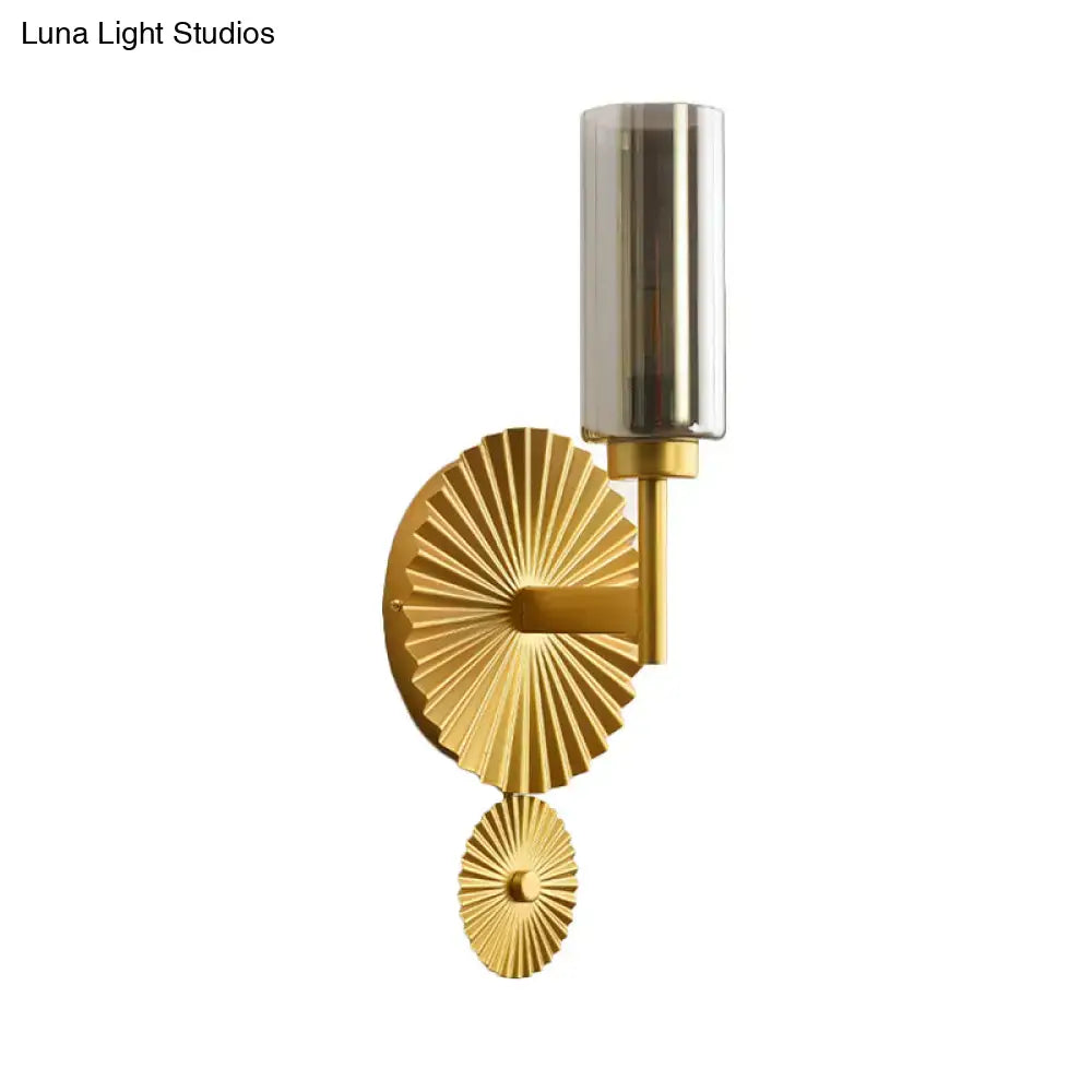 Gold-toned mid century brass wall sconce with scalloped backplate and amber cylindrical glass shade for bedroom use