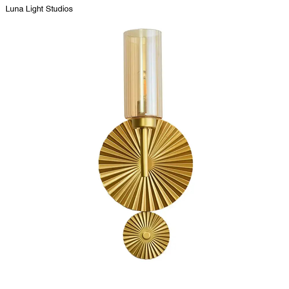 Mid century brass wall sconce with scalloped backplate, gold-toned finish, cylindrical amber glass shade, and fan-like discs