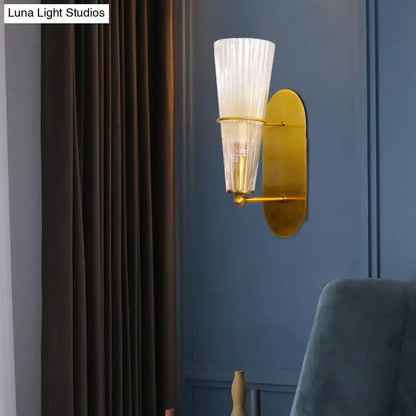 Mid century brass wall lamp with gold-toned fixture and clear ribbed glass single light for bedroom use