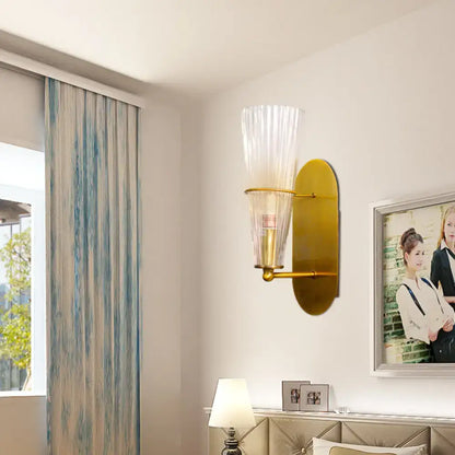 Mid century brass wall lamp with gold-toned finish and clear ribbed glass single light for bedroom use