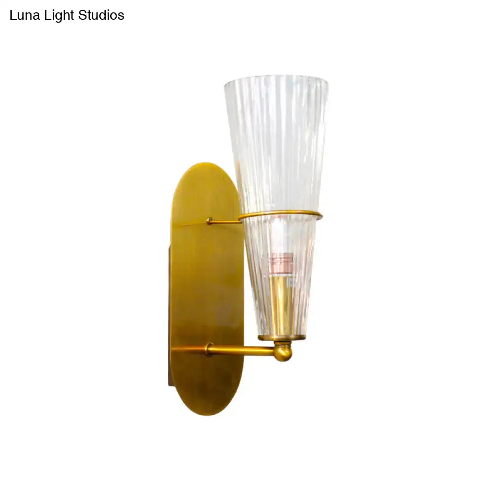 A sleek mid century wall lamp with a brass finish and clear ribbed glass single light shade for bedroom use