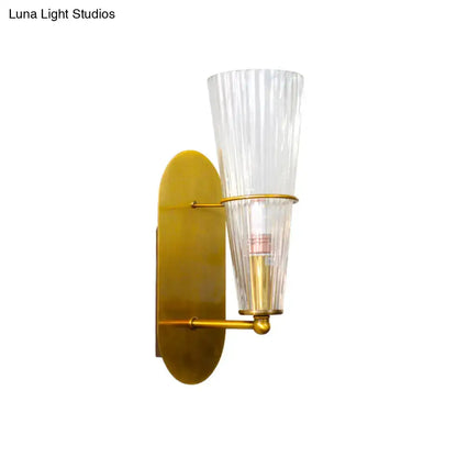 A sleek mid century wall lamp with a brass finish and clear ribbed glass single light shade for bedroom use