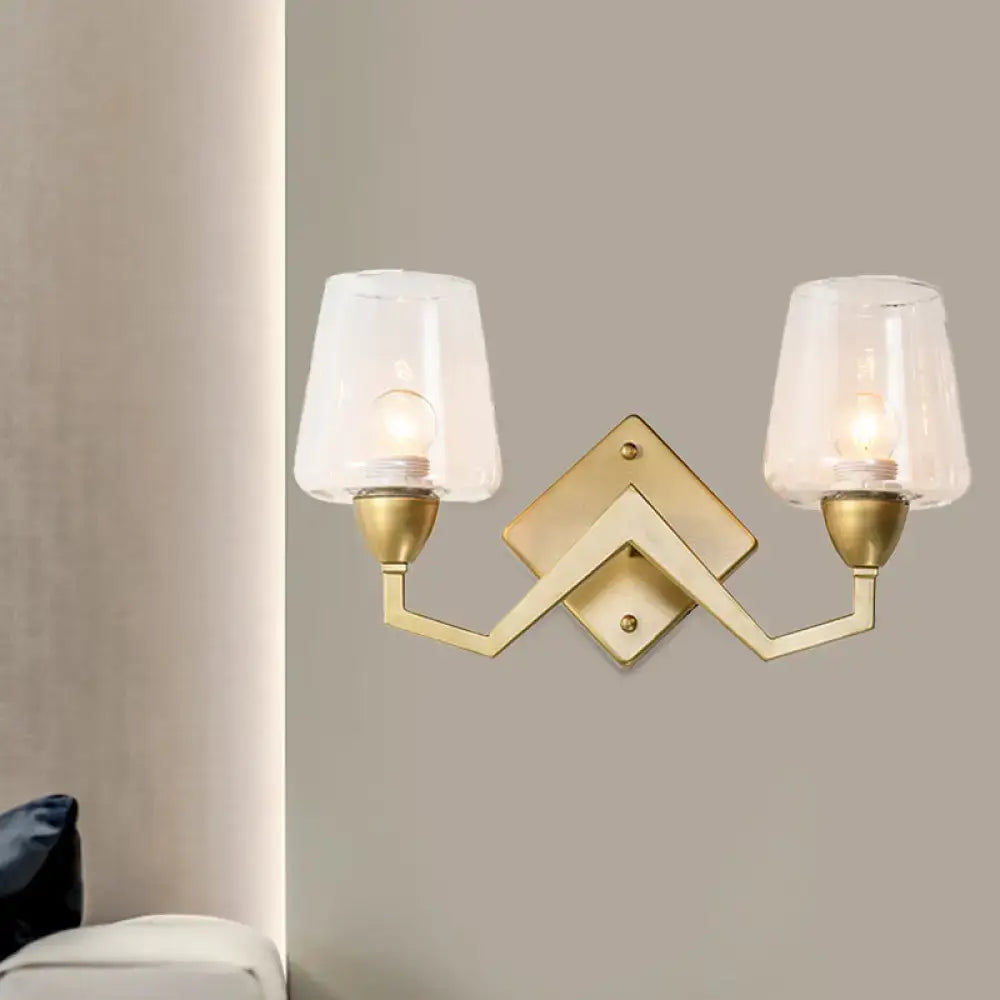 Gold-toned mid-century brass wall lamp with truncated cone shade and two frosted glass shades for bedroom lighting