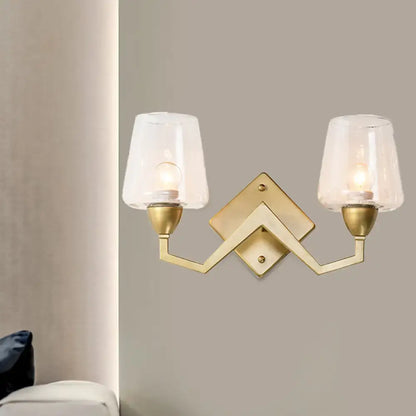 Gold-toned mid-century brass wall lamp with truncated cone shade and two frosted glass shades for bedroom lighting