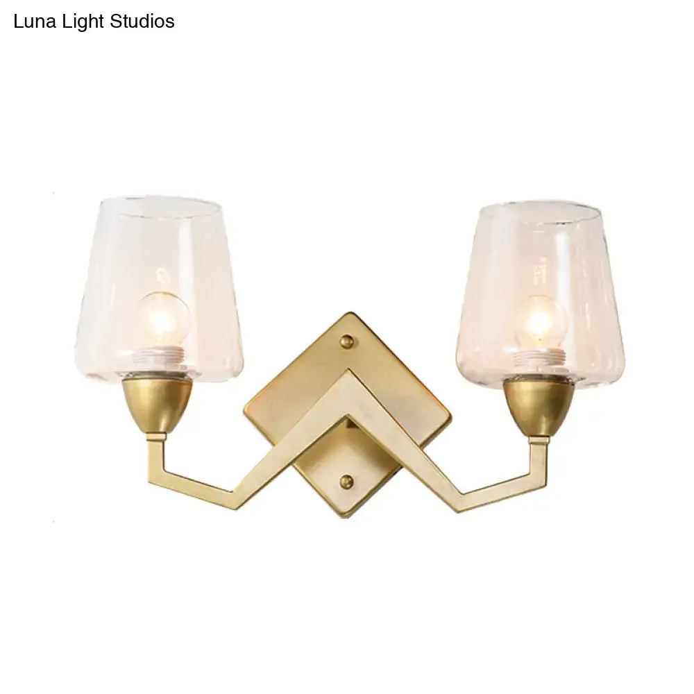 Gold-toned mid-century wall lamp with brass frame and two clear truncated cone shades for bedroom lighting