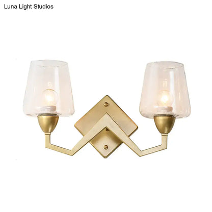 Gold-toned mid-century wall lamp with brass frame and two clear truncated cone shades for bedroom lighting
