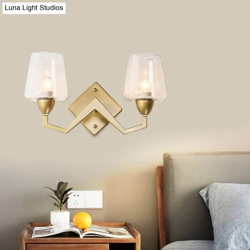 Brass-finished mid-century wall lamp with double arms and clear glass truncated cone shade for bedroom lighting