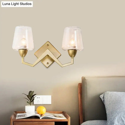 Brass-finished mid-century wall lamp with double arms and clear glass truncated cone shade for bedroom lighting