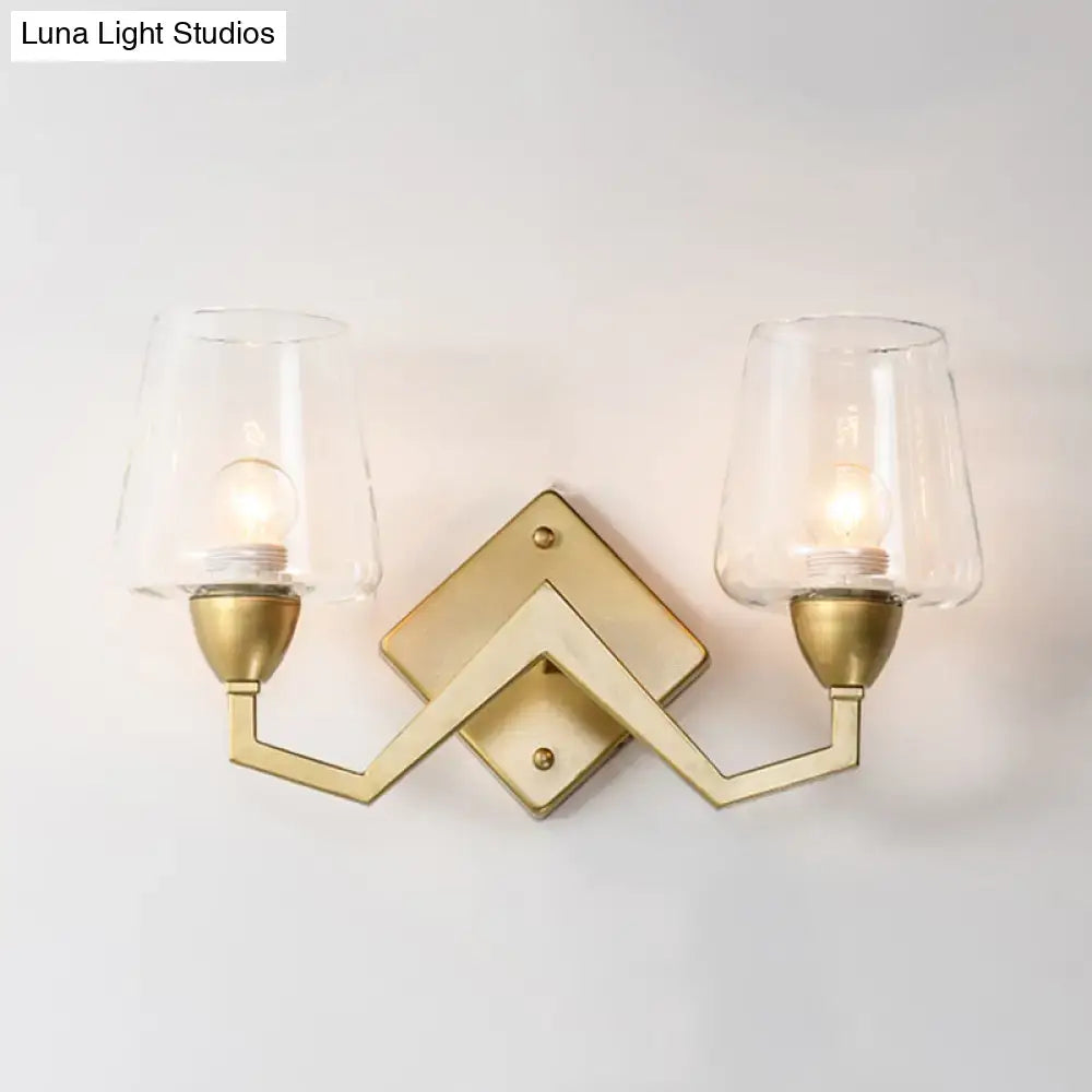 Gold-toned mid-century wall lamp with truncated cone shades and clear glass for bedroom lighting