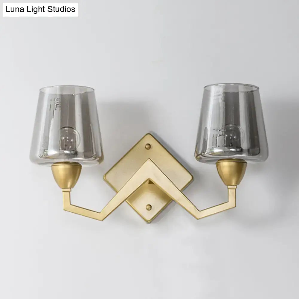 Gold-toned mid-century brass wall lamp with geometric design and two smoked glass truncated cone shades for bedroom use