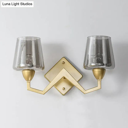 Gold-toned mid-century brass wall lamp with geometric design and two smoked glass truncated cone shades for bedroom use