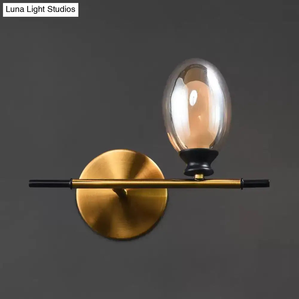 Mid century gold and black wall lamp with sleek rod and oval amber glass shade ideal for bedroom lighting