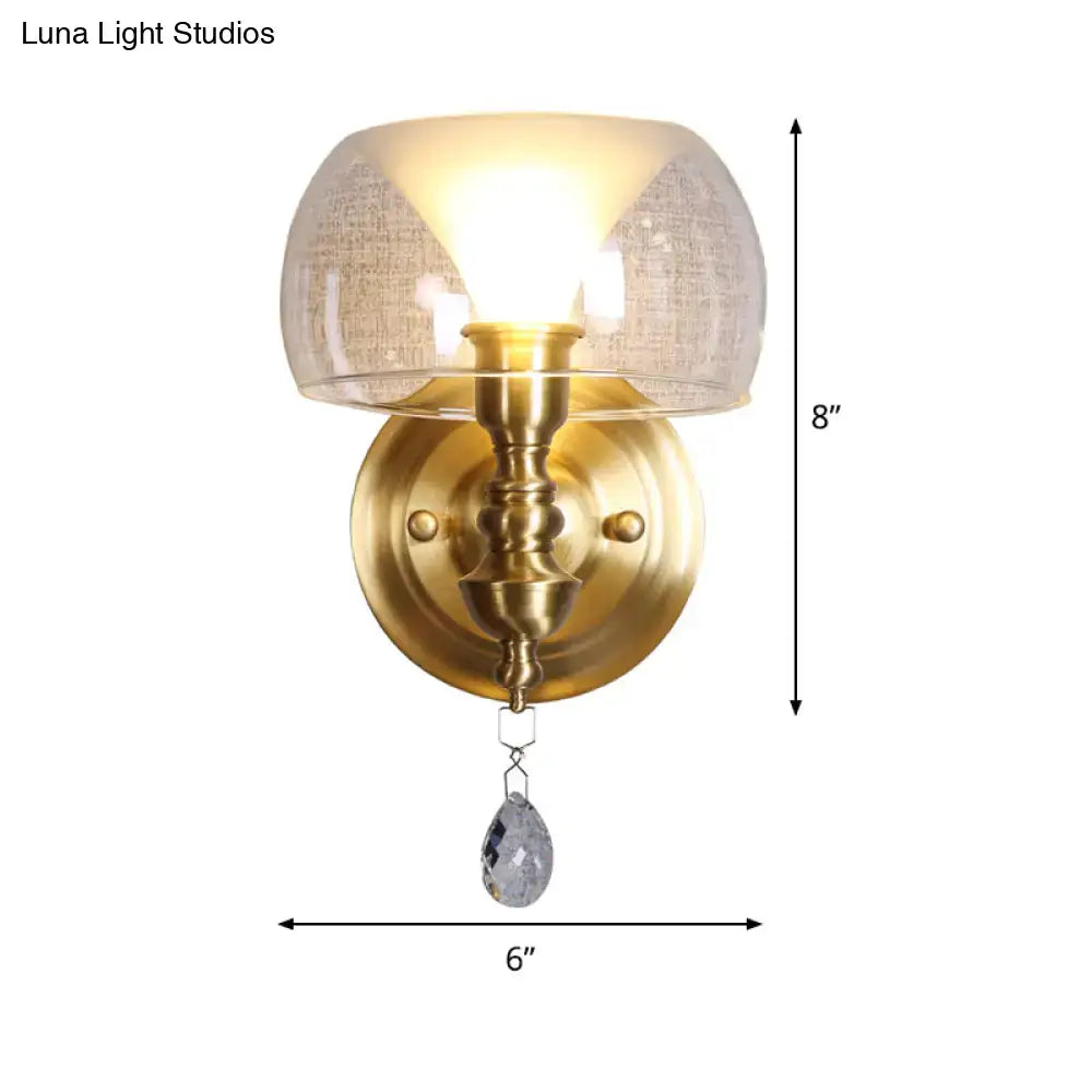 Mid century antique brass wall sconce with a textured flared glass dome and hanging crystal droplet for bedroom use