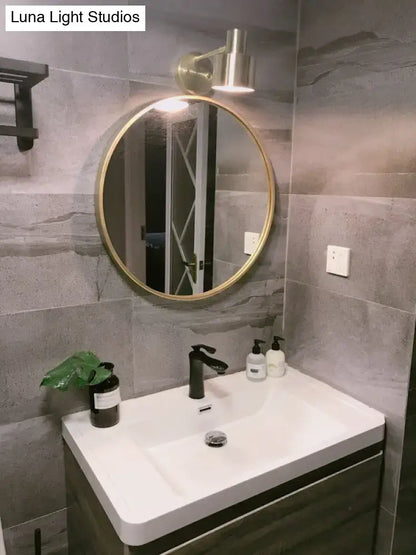 Round gold-framed mirror with modern design mounted above white sink vanity in mid-century gold metal cage home wall lighting