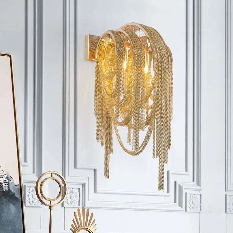 Gold-toned mid century wall lamp with silver stacked tassel chain links and modern sculptural design for bedroom sconce