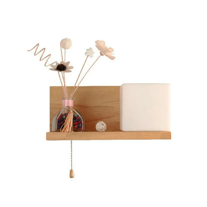 Milk glass cube wall light with light wood floating shelf holding a glass reed diffuser and white ceramic lamp