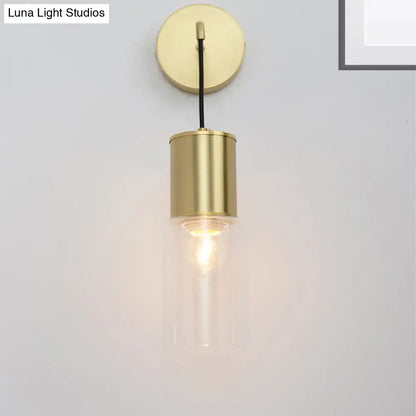 Minimal brass and glass wall sconce light with cylindrical design and exposed filament bulb for bedroom use