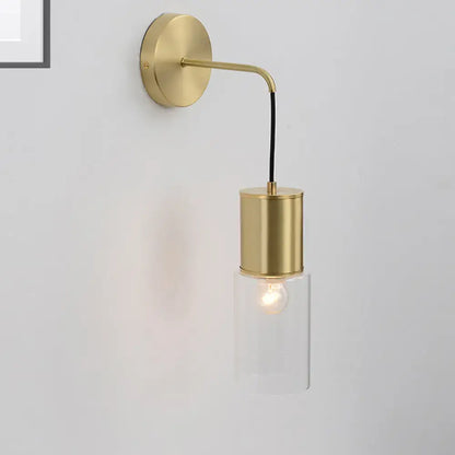 Minimal brass and glass wall sconce light with a gold-toned curved arm and clear glass cylinder housing an exposed bulb