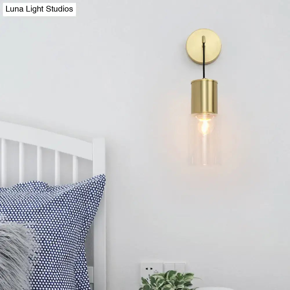 Minimal brass and glass wall sconce light with gold-toned cylindrical design and exposed filament bulb for bedroom use
