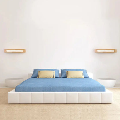 White tufted platform bed with blue bedding and beige pillows under minimalist bamboo led nordic style wall sconce lighting