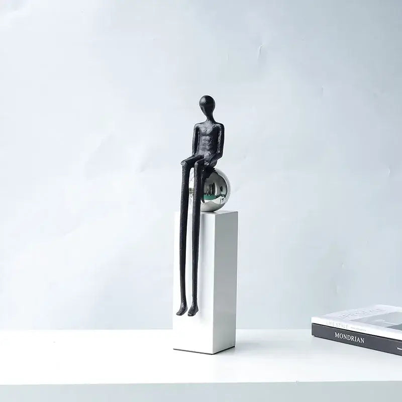 Minimalist black metal figurine with elongated limbs seated on a reflective silver sphere for decorbites abstract thinker decor