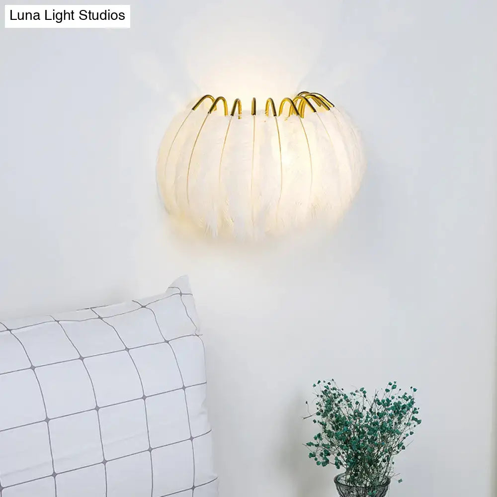 A minimalist black and gold feather wall sconce with soft white feathers and a gold-toned metal frame light type fixture height