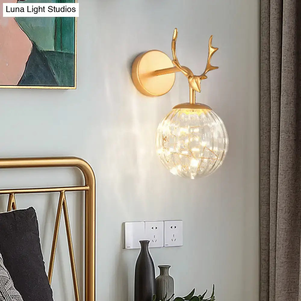 Gold-toned deer-head wall sconce with faceted clear glass globe and warm led lights for minimalist bedroom decor