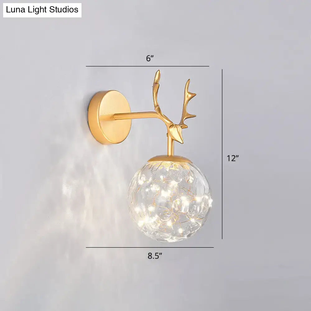 Minimalist gold-toned deer antler wall sconce with clear glass globe and warm white LED lights for bedroom fairy lighting