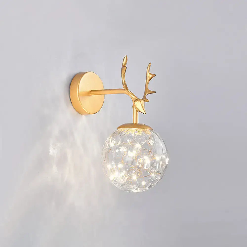 Gold-toned deer-head wall sconce with clear textured glass globe housing warm LED lights for minimalist bedroom décor