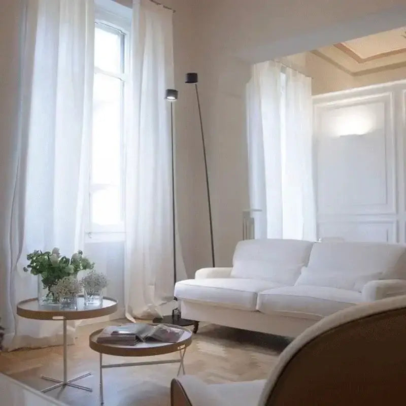 White upholstered sofa with clean lines and soft cushions next to minimalist decorbites black floor lamp with curved led arms
