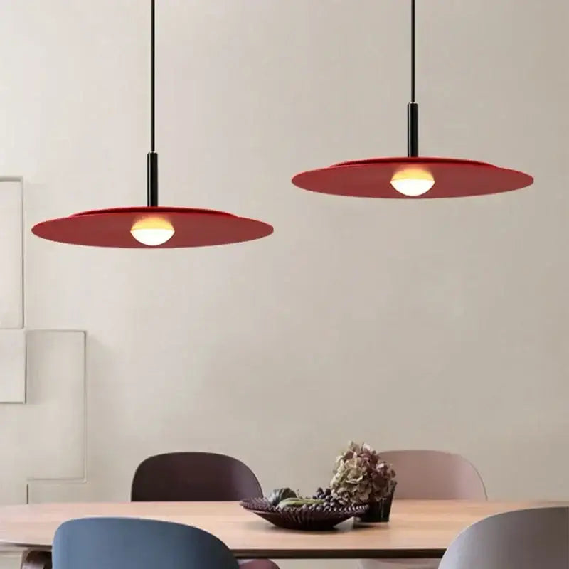 Two modern red decorbites flying saucer led pendant lights with black cords hang above a dining table