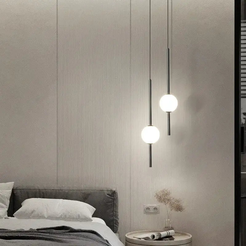 Two minimalist black globe pendant lights with frosted glass shades and slender rods for cord pendant installation