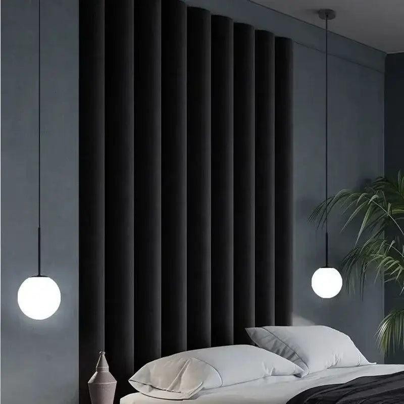 Minimalist black and gold globe pendant light with led bulb and matte white glass shades hanging above a bed