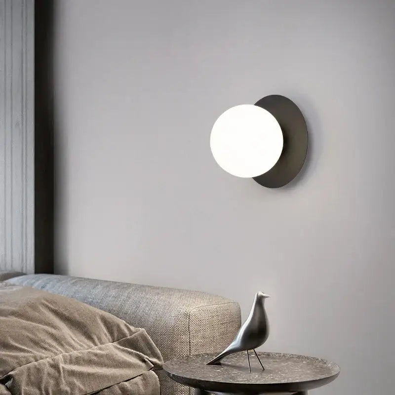 Minimalist black and gold led wall sconce with matte black base and glowing white glass globe for bedroom lighting
