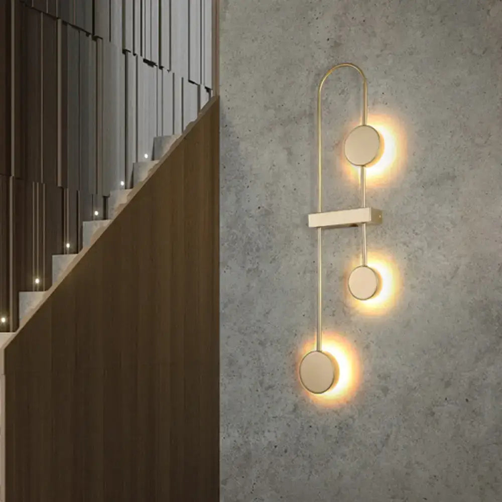 Minimalist black gold metal led wall sconce with three circular lights on a curved frame for bedroom lighting