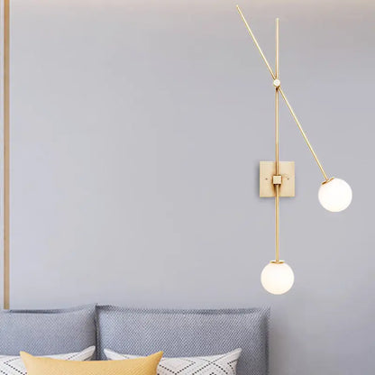 Gold-toned bedroom wall sconce light fixture with slender metal arms and two opal glass bubble frosted shades