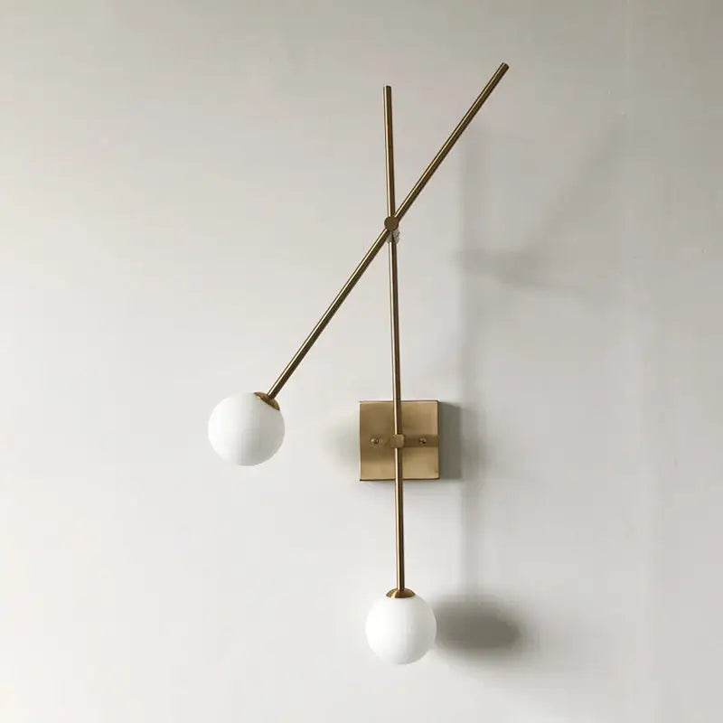 Minimalist black and gold metal arm light fixture with two white opal glass bubble shades for bedroom sconce