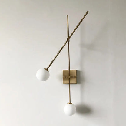 Minimalist black and gold metal arm light fixture with two white opal glass bubble shades for bedroom sconce