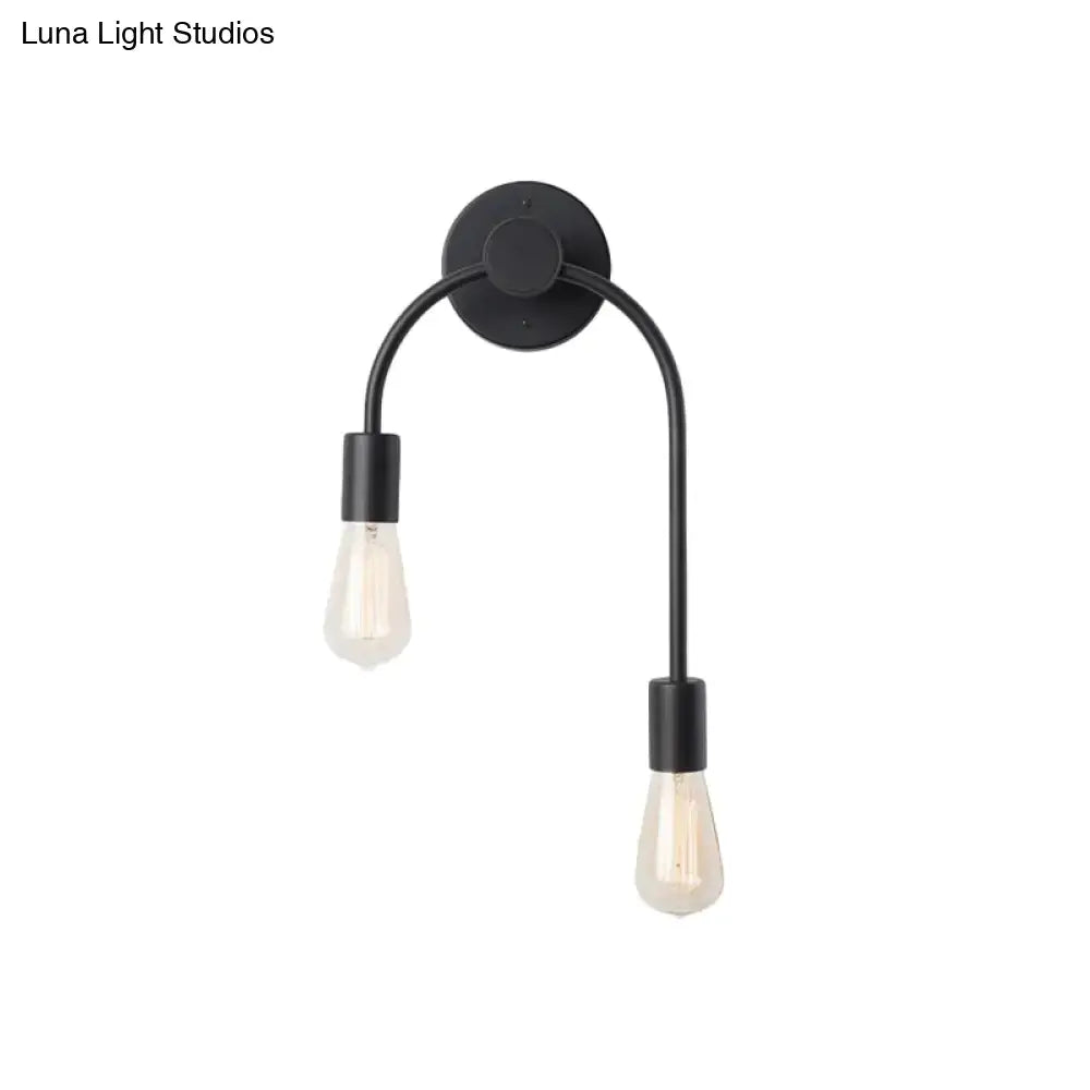 Minimalist black metal wall lamp with gold accents and double curved arms holding clear filament bulbs for bedroom use
