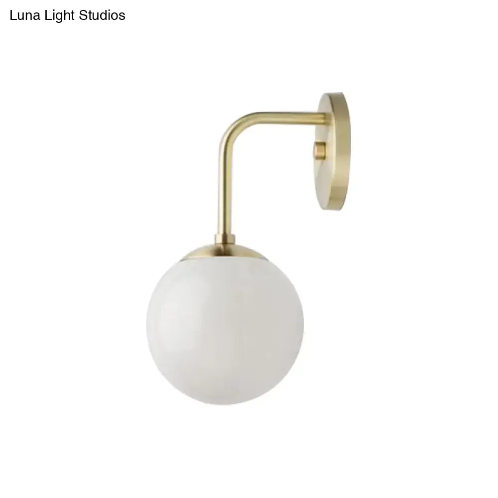 A minimalist golden black wall light with brass finish and milky glass ball shade for bedroom lighting